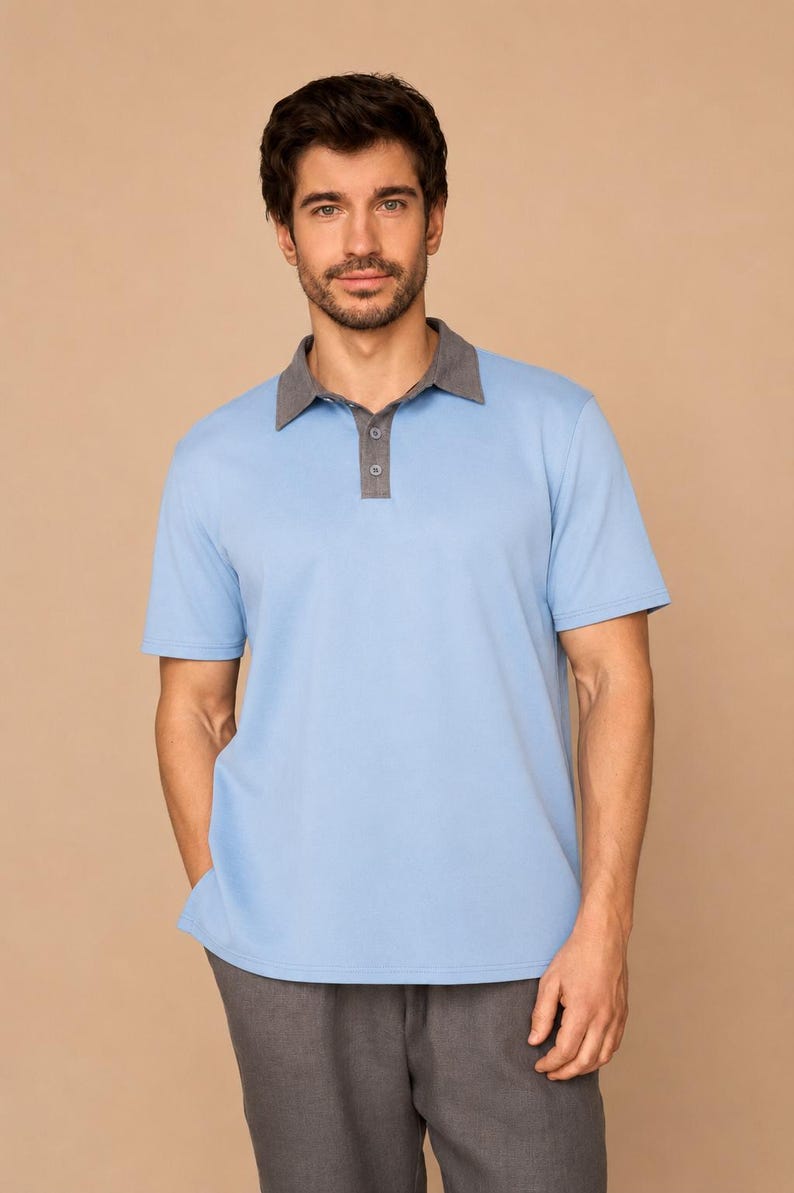 May include: A short-sleeved polo shirt in light blue featuring a contrasting dark gray collar and a buttoned placket. The shirt is paired with dark gray trousers, creating a two-toned ensemble with a clean, structured appearance and simple design.