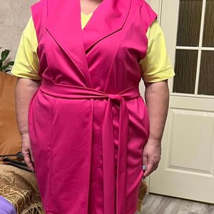 K&ouml;nnte beinhalten: Eine rosa &auml;rmellose Weste mit einem breiten Kragen und einem passenden G&uuml;rtel. Die Weste ist aus einem weichen, dehnbaren Stoff gefertigt und hat eine lockere Passform.