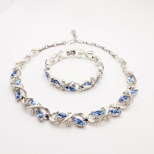 May include: A silver necklace and bracelet set with blue crystal accents. The necklace and bracelet feature a delicate, twisted design with marquise-shaped crystals.