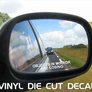 Puede incluir: Espejo retrovisor de coche que refleja una carretera con un coche delante. El texto "OBJECTS IN MIRROR ARE LOSING" es visible. Las palabras "VINYL DIE CUT DECAL" están en la parte inferior.