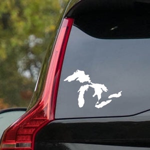 May include: White vinyl decal of the Great Lakes on a car window. The decal shows the outline of the five Great Lakes: Superior, Michigan, Huron, Erie, and Ontario. The decal is applied to the rear window of a black vehicle.