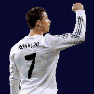 Puede incluir: Una camiseta de fútbol blanca con ribetes negros y el nombre "RONALDO" y el número "7" impresos en la espalda. El jugador levanta su brazo derecho en el aire.