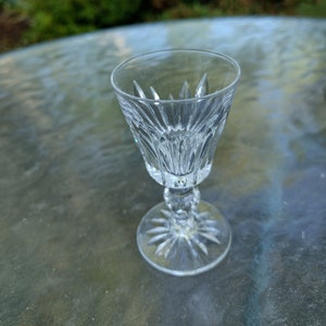 May include: A clear, cut-glass cordial glass with a starburst base and a decorative stem. The glass has a flared bowl with vertical cuts and is designed for serving small portions of liquor or dessert wine.