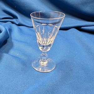 May include: A clear, stemmed glass with a flared bowl and a round base. The glass has etched patterns on the bowl. The stem has a bulbous design. The glass is likely for serving a beverage.