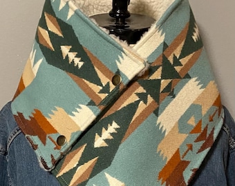 Puede incluir: Un calentador de cuello turquesa y crema con un patrón geométrico en tonos marrón, verde y beige. El interior está forrado con un suave forro polar color crema. El calentador de cuello se asegura con dos botones dorados.