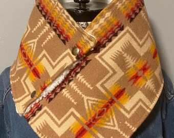 Könnte beinhalten: Ein brauner und cremefarbener Halswärmer mit einem geometrischen Muster in Rot, Orange und Gelb. Der Halswärmer hat ein weiches, weißes Kunstfellfutter und wird mit zwei goldfarbenen Druckknöpfen befestigt. Der Halswärmer wird auf einem schwarzen Schaufensterpuppenkopf präsentiert.