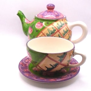 May include: A green and purple tea set with a teapot, cup, and saucer. The teapot has a floral design and the cup and saucer have a checkered pattern.