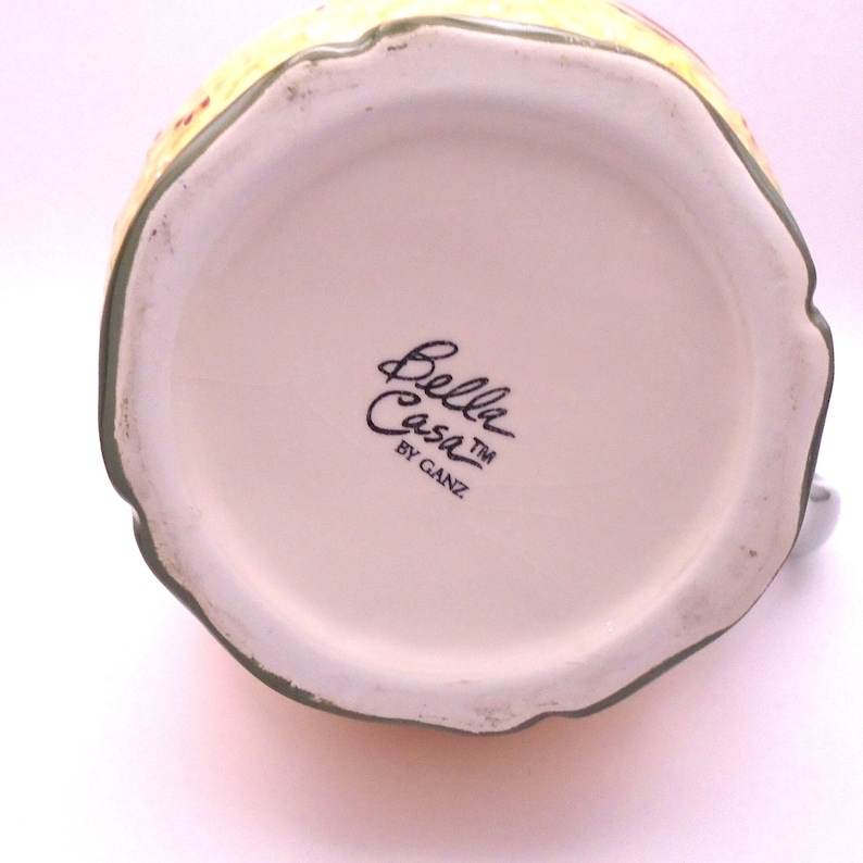 May include: The bottom of a ceramic pitcher with a green rim and a black and white logo that reads "Bella Casa TM by Ganz".