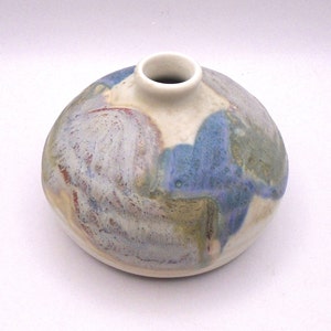 May include: A small, round ceramic vase with a white glaze and blue, green, and brown abstract patterns.