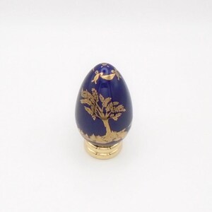 May include: A small blue and gold porcelain egg with a gold tree design. The egg is on a gold stand.