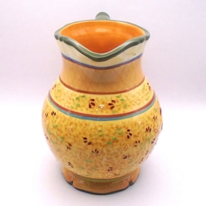 May include: A yellow ceramic pitcher with a green rim and floral pattern. The pitcher has a wide mouth and a handle.