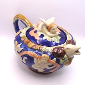 May include: A blue and white ceramic teapot with a cherub on the lid and a dolphin spout. The teapot is decorated with cherubs and floral designs.
