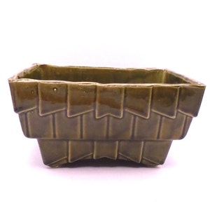 May include: A green ceramic planter with a geometric design. The planter has a rectangular shape with a slightly flared rim and a base with four feet.
