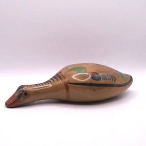 May include: A hand-painted ceramic bird figurine with brown, black, orange, and green accents. The bird is lying on its side with its head turned to the left.