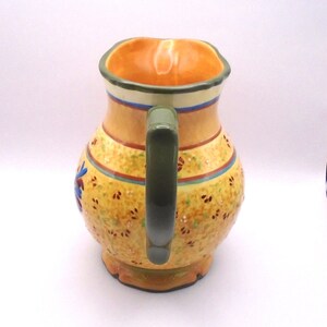 May include: A yellow ceramic pitcher with a green handle and a floral design. The pitcher has a wide mouth and a rounded body.