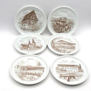 May include: Set of six white ceramic coasters with brown illustrations of buildings and landscapes from the town of Goettingen, Germany. Each coaster features the text "Goettingen" and the name of a specific location.