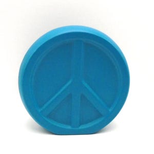 May include: A round, blue peace sign made of ceramic. The peace sign is raised in relief.