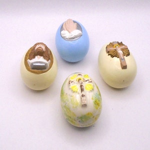 May include: Four decorative Easter eggs with religious themes. One egg is light blue with a pair of hands in prayer. Another egg is white with a yellow and brown cross. The third egg is white with a yellow and brown cross and a floral design. The fourth egg is white with a depiction of Jesus.