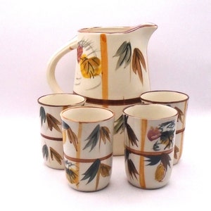 May include: A set of five ceramic cups and a pitcher with a white background and a brown, yellow, and green floral pattern.