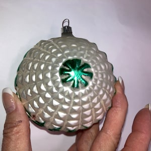 May include: A white glass Christmas ornament with a green star design. The ornament has a textured surface and a silver hanger.