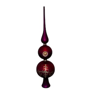 May include: A decorative Christmas tree topper in a deep red and purple color scheme. The topper features a long, pointed finial above two round, ornate bulbs. Gold glitter accents the design, adding a festive touch.