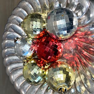 Op de afbeelding: Een zilveren dienblad met zes discoballen. De ballen zijn in tinten goud, zilver en rood.