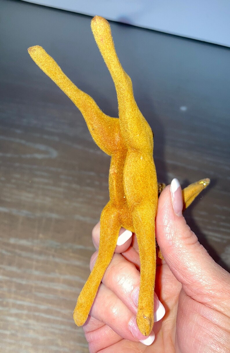 Pode incluir: Uma figura de rena vintage de feltro amarelo com uma cauda de glitter dourado. A rena est&aacute; em p&eacute; sobre suas patas traseiras com as patas dianteiras levantadas no ar.