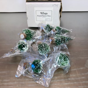 May include: A set of eight frosted topiary trees, each individually packaged in plastic bags. The trees are green with white frosting and come in a white box labelled "Village Frosted Topiary Trees".