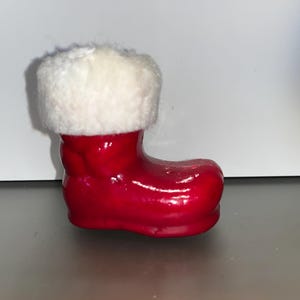 May include: A small red and white Santa boot ornament. The boot is shiny and has a white fur trim.