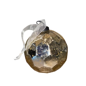 Könnte beinhalten: Ein facettierter, goldfarbener Weihnachtsschmuck mit gesprenkelter Oberfläche. Der Schmuck hat eine schwarze Kappe und wird von einem durchsichtigen, weißen Band gehalten. Die kugelförmige Dekoration ist für Weihnachtsbaumausstellungen gedacht.