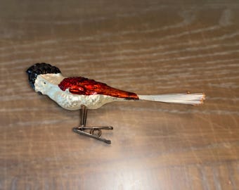 Può includere: Un ornamento di uccello in vetro bianco con accenti rossi e neri. L'uccello ha una lunga coda di piume bianche e una clip di metallo per appenderlo.