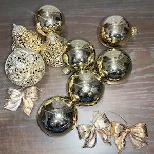 Op de afbeelding: Een verzameling gouden kerstversieringen, waaronder ronde kerstballen, een bel en een strik. De versieringen zijn allemaal glanzend en hebben een metallic afwerking.