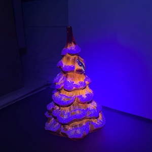 May include: A ceramic Christmas tree figurine with a brown and white glaze. The tree is decorated with white, sparkly details and has a rounded, tiered shape.
