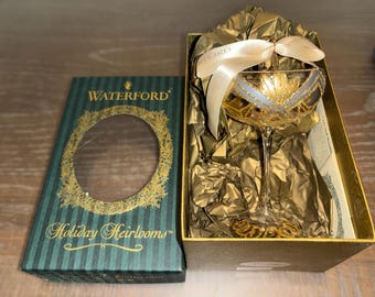 以下が含まれることがあります： ゴールドとシルバーのアクセントが施されたシャンパングラスの形をしたウォーターフォードホリデーヘリロームのオーナメント。オーナメントは緑と金のデザインの箱に入っています。