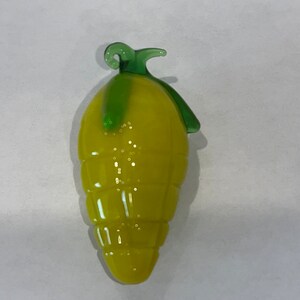 May include: A yellow glass lemon with a green glass stem. The lemon has a textured surface and is shaped like a real lemon.