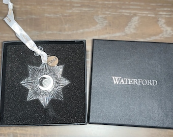 May include: A Waterford crystal star ornament in a black box with a silver tag that says "2014". The box is labeled "Waterford" in silver lettering.