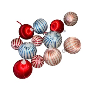 Puede incluir: Una colección de adornos navideños de varios tamaños y diseños. Los adornos presentan una mezcla de colores rojo, blanco y azul, con patrones a rayas y lisos. Cada adorno tiene un pequeño lazo para colgar.