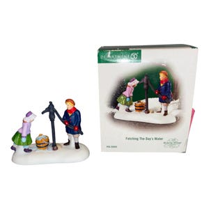 May include: A Department 56 Dickens Village figurine titled Fetching The Day's Water, featuring two figures in winter clothing at a water pump with a wooden bucket, accompanied by its original white cardboard box with product imagery.
