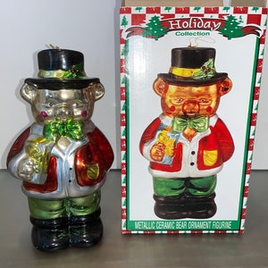 May include: A ceramic bear ornament figurine wearing a red and green suit, a black top hat, and holding a gift. The ornament is metallic and has a gold trim. The box reads "Holiday Collection" and "Metallic Ceramic Bear Ornament Figurine".