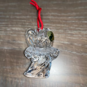 Op de afbeelding: Een helder glazen engel ornament met een rood lint en het woord "Remember" op een banner. Het ornament is gemaakt door Waterford.