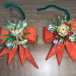 May include: Two orange felt Christmas decorations with green and silver sprigs, red berries, and gold accents. One decoration features a gold bird figurine, while the other has a gold star.