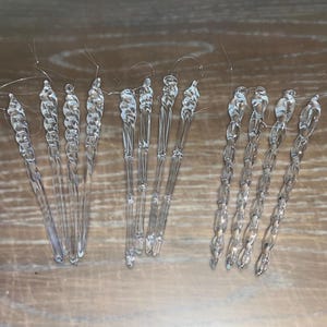 May include: A set of 12 clear glass icicle ornaments with a twisted design. The ornaments are approximately 6 inches long and have a silver wire loop at the top for hanging.