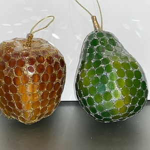 Pode incluir: Dois enfeites de Natal em forma de fruta. O primeiro enfeite é uma maçã marrom dourada com acabamento brilhante. O segundo enfeite é uma pêra verde com acabamento brilhante.