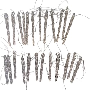 May include: An overhead shot shows multiple silver-colored, elongated objects with looped strings attached. The objects are arranged in two rows against a white background. The objects appear to be metallic and have a textured surface.