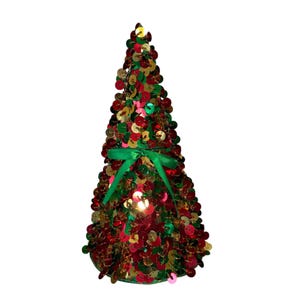 May include: A decorative Christmas tree covered in red, green, and gold sequins. A green ribbon is tied around the middle of the tree. The tree is cone-shaped and stands on a white background.