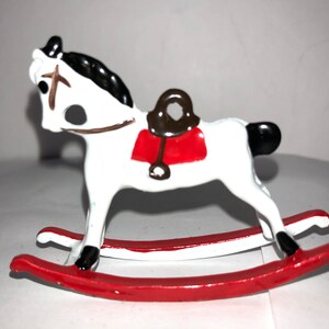May include: White rocking horse toy with a red saddle and black mane and tail. The rocking base is red.
