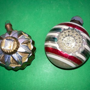May include: Two vintage glass Christmas ornaments. One is silver with a gold star design and the other is white with red and green stripes.