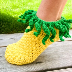 May include: A yellow and green crochet sock resembling a pineapple. The sock features a textured yellow body and a green, tentacle-like design around the ankle. The sock is handmade and appears to be comfortable.