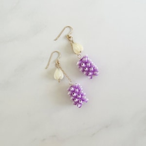 May include: A pair of earrings with a white flower charm and a cluster of purple and white flower-shaped beads.