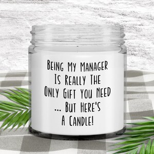 Op de afbeelding: Een witte kaars in een glazen pot met een zwart etiket waarop staat: "Manager zijn is echt het enige cadeau dat je nodig hebt... maar hier is een kaars!"